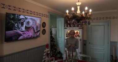 Kadın masadaki mumları yakıyor. Bu evde güzel Noel süsleri, iyi ışıklandırılmış bir ağaç, süsler ve şık bir yemek düzeneği sergileniyor. Tatil ortamı.