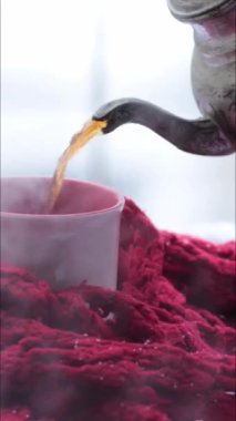 Süslü metal çaydanlıktan kırmızı eşarba sarılı fincana sıcak çay dökmek ve kardan yükselen buhar. Geleneksel desenli Arap tarzı klasik metal çaydanlık. Dikey biçim videosu