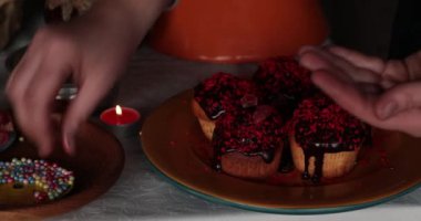 Parmaklar çikolatalı kek süslemesi için renkli boncuklar alır. Cadılar Bayramı çörekleri masada, üzerinde yanan çay ışığı mumu ve klasik sofra takımı var. Cadılar Bayramı ziyafeti pişirme