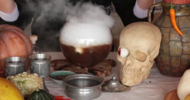 Kadın cadı sihirli iksiri cam kaseye koyup Cadılar Bayramı süslemeleri ve kafatası ile masaya koydu. Gizemli gotik kadın sihirli iksirle büyü yapıyor. Cadılar Bayramı iksiri yapma konsepti. Boom görünümü