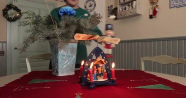 Kadınlar Noel sofrasını mum yel değirmeni ve retro fındıkkıranlarla süslerler. Kış tatili için Xmas yemeği dekorasyonu. Klasik stil geleneksel Noel süslemeleri masa örtüsü.