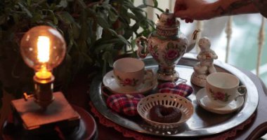 Eller eski çaydanlıkta çay yapar. Süslü fincanlar, büyüleyici bir çaydanlık ve tatlı ikramlarla harika çay saatleri başlıyor. Dekoratif detaylarla klasik çay saati ayarları 