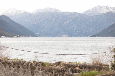 Sakin bir körfezin üzerindeki görkemli dağlar, sakin sulara sabah ışığını yansıtırken, uzak bir kıyı şeridi Karadağ 'ın barışçıl doğasını ortaya koyuyor.
