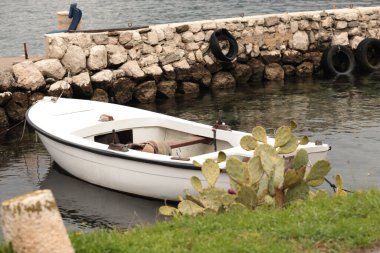 Small white boat is gently resting by a sturdy stone pier, its reflection visible in the calm waters. clipart