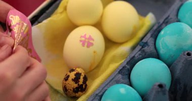 Paskalya yumurtalarını çıkartmalarla süsleme işlemi. Bu eğlenceli etkinlik, renkli tasarımlar ve eşsiz dekorasyonlara odaklanarak mavi ve sarı renkli yumurta boyama adımlarını gösteriyor..