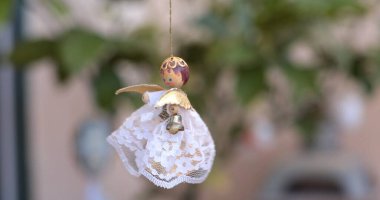 Güzel bir dantel etek ve altın aksanla ince bir ipten sarkan el yapımı bir melek süslemesi. Parlak yeşillik, barışçıl bir ortam yaratmak için bir zemin görevi görüyor..