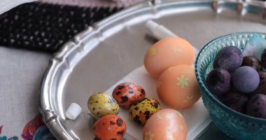 Renkli inci boyalı Paskalya yumurtaları gümüş bir tepside, daha küçük benekli yumurtaların yanında duruyor. Renkli yumurta aktiviteleriyle yapılmış çeşitli tasarımlar sergiliyorlar..