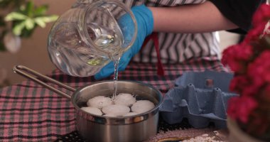 Su, içinde yumurta olan bir tencereye dökülüyor, kaynamaya hazırlanıyor. Bu etkinlik, dekorasyon ve kutlama için renkli Paskalya yumurtaları yapma sürecinin bir parçasıdır..
