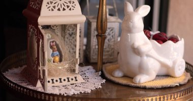 Çok güzel düzenlenmiş bir bahar evi dekorasyonu sergisinde seramik bir tavşanın yanında Paskalya heykelciği tutan dekoratif bir fener bulunur..