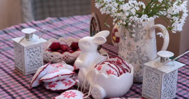 İlkbahar çiçekleri büyüleyici bir masa ortamında sergilenen Paskalya süslemelerini güçlendirir. Beyaz tavşan heykelciği ve çiçek aranjmanları bayram neşesi getirir, mevsimlik kutlamalar için mükemmeldir..