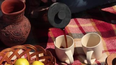 Kadın beyaz kupalara sıcak kahve döker, sonra da kil sürahide süt ekler. Açık hava pikniği taze elmalarla dolu bir sepete odaklanıyor. 