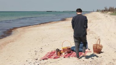 İki kadın, doğanın güzelliğiyle çevrili bir piknik düzeniyle plajda dinleniyor. Birlikte güzel vakit geçiriyorlar. Sevgi, çeşitlilik ve mutluluk gösteriyorlar..