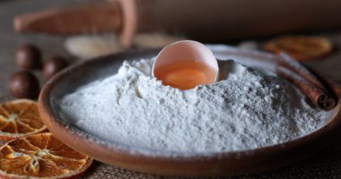 Kırık yumurta kabuğunun içinde beyaz un ve yumurta sarısı ile ev yapımı pişirme için organik gıda içerikli yiyecek. Geleneksel ahşap kasede un yığını. Kurutulmuş portakal dilimleri ve tarçın.