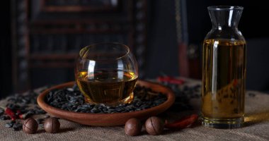 Yuvarlak cam kase, fındık ve kurutulmuş kırmızı biberlerle çevrili siyah tohumlarla dolu ahşap bir tabağa yerleştirilmiş sıcak yağ içerir. Toprak ve kırsal bir atmosfer yaratır..