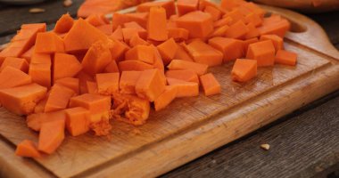 Taze doğranmış balkabağı parçaları ahşap kesim tahtasının üzerinde duruyor. Çeşitli yemek uygulamaları için mükemmel. Parlak turuncu renk, sonbahar şenliklerinde mevsimsel esansı vurguluyor.