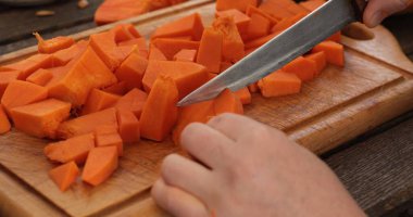 Parlak turuncu balkabağı parçaları ustalıkla cilalanmış ahşap kesme tahtasıyla doğranır. Sabah ışığında keskin bıçak parıldıyor, sıcak mutfakta sonbahar tarifleri için malzemeleri hazırlıyor..