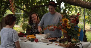 Bir grup arkadaş ve aile, Şükran Günü yemeğinde mevsimlik yemekler ve taze ürünlerle dolu güzel bir masanın etrafında toplandı..