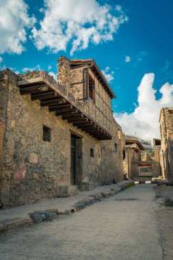 Pompeii, İtalya 'da tarihi taş evleri olan tarihi bir kaldırım taşı caddesi, parlak mavi gökyüzünün altında tüylü beyaz bulutlar, antik Roma şehrinin kalıntılarını sergiliyor..