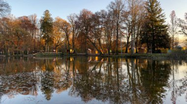 Günbatımında Sükûnet Sonbahar Gölü Yansıyan Renkli Ağaçlar. Sakin bir sonbahar gölü güzel bir şekilde renkli ağaçları ve batan güneşin sıcacık parıltısını yansıtır. Huzurlu sahne mevsimleri yakalar