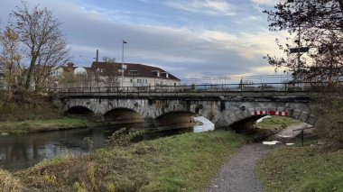 Taştan Köprü, Sakin Nehir Mangfall ve Idyllic Taşra Ayarları ve Bulutlu Gökyüzü. Tarihi bir taş köprü, yemyeşil ve eski binalarla çevrili sakin bir nehri kapsar. Bulutlu gökyüzü