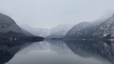 Avusturya 'nın Hallstatt şehrinde kar kaplı dağlarla çevrili Serene Misty Dağı Yansıması. Puslu dağ gölü Hallstatt. Durgun su karla kaplı tepeleri yansıtıyor.