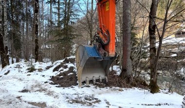 Kış Ormanı Ormanı 'ndaki Kar Kapaklı Turuncu İnşaat Kazıcısı. Bir turuncu inşaat kazıcısı, ağaçlarla çevrili, karlı bir ormanlık alana park edilmiş ve güzel bir kış manzarası var.
