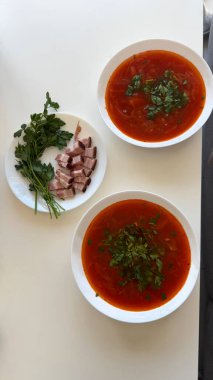 Domuz yağı ve taze maydanozlu geleneksel Ukrayna Borscht 'u. Beyaz bir masada servis edilen iki kase geleneksel Ukrayna çorbası. Canlı kırmızı pancar çorbası tazeyle süslenir.