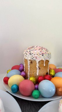 Renkli süslemelerle süslenmiş Paskalya pastası canlı yumurtaların arasında, bahar şenlikleri ve sağlıklı beslenme konsepti için neşeli bir kutlama atmosferi yaratıyor.