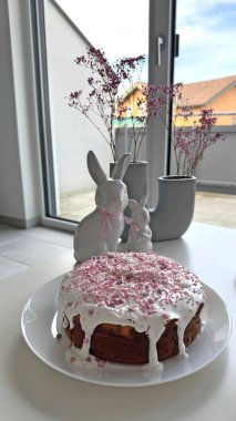 Süslü Paskalya pastası, bir tabağa konur ve yanında büyüleyici tavşan figürleri ve zarif çiçek aranjmanları vardır. Kutlamalar için hoş bir atmosfer yaratır.