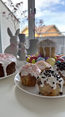 Renkli krema ve şekerlerle süslenmiş pastalar bir masada sergilenirken, festival dekorasyonları ve Paskalya temalı unsurlarla birlikte bahar kutlamaları için canlı bir atmosfer yaratılıyor.
