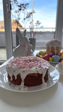 Süslü ve renkli paskalya pastası Paskalya süslemeleriyle süslenmiş bir masanın üzerinde duruyor. Sevimli bir tavşan figürü, renkli ve çikolatalı yumurta.