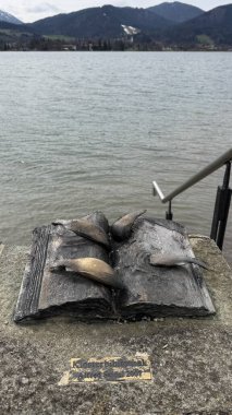 Tegernsee, Almanya - 30 Mart 2025: Bavyera Gölü yakınlarındaki açık kitap heykelinde dağlar ve doğal güzellikler arasında yer alan balıklar yer alıyor. Seyahat blogları için mükemmel.