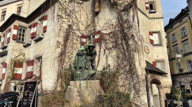 Innsbruck, Avusturya - 28 Mart 2025: Renkli panjurlu eski Avrupa binası, geleneksel bir mimari tarzı, iki kişinin bronz heykeli, Christian Platter tarafından yaratılan Anıt 9 olarak bilinir.