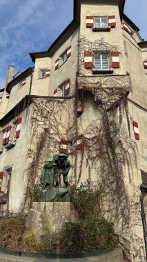 Innsbruck, Avusturya - 28 Mart 2025: Sarmaşık örtülü duvarlar, kırmızı-beyaz panjurlar ve Christian Platter tarafından yaratılan ve Anıt 9 olarak bilinen iki kişinin bronz heykeli ile süslenmiş tarihi bina