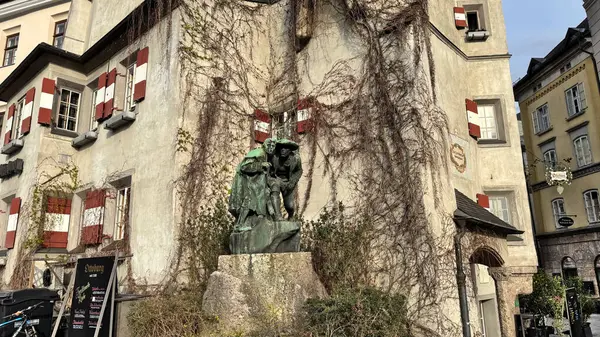 Innsbruck, Avusturya - 28 Mart 2025: Renkli panjurlu eski Avrupa binası, geleneksel bir mimari tarzı, iki kişinin bronz heykeli, Christian Platter tarafından yaratılan Anıt 9 olarak bilinir.