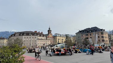 Innsbruck, Avusturya - 28 Mart 2025 Innsbruck şehir meydanı insanlarla dolup taşıyor, tarihi mimari ve çarpıcı dağ manzaraları, kentsel yaşamı gözler önüne seriyor