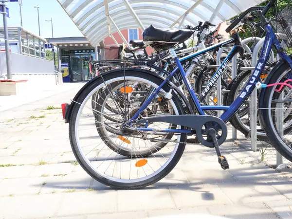 31.05.2025 Almanya: Şeffaf bir tepe örtüsünün altındaki Açık Hava Bisiklet Rafında park edilmiş bisikletler. Modern bir açık çatı altında güvenli bir yere park edilmiş çoklu bisikletler, şehir merkezini gösteriyor.
