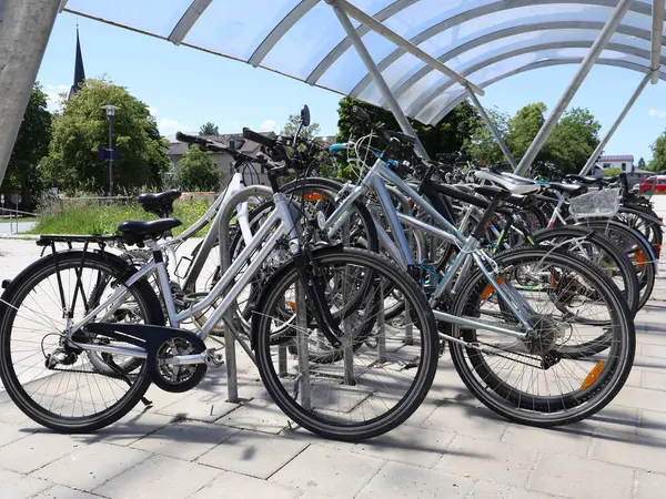 Bir grup bisiklet, güneşli bir günde modern bir gölgelik altında tren istasyonuna park etti. Bisikletler kapalı bir bisiklet parkında güvenli bir şekilde park edilmiş ve manzaralı arka planı var..