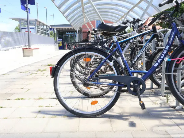 31.05.2025 Almanya: Tren istasyonunda kapalı bisiklet parkında park edilmiş bisiklet sırası. Kapalı bir alanın altına park edilmiş, temiz gökyüzüne sahip kentsel bir arka plan içeren bir bisiklet koleksiyonu. Görüntü