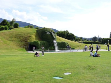 01.06.2025 Avusturya: Avusturya 'nın Wattens kentindeki Swarovski Kristallwelten Kristallwelten kentindeki ikonik dev şelalenin önünde dinlenen turistler. Çimenlerle kaplı, akan suyla birlikte heykel