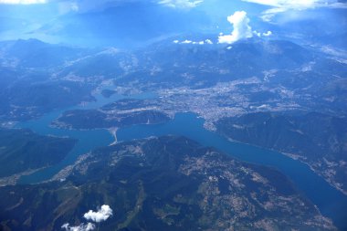 Güneşli havada dağlarla ve köylerle çevrili Sersemletici Göl 'ün Hava Manzarası. Yüksek irtifa görüntüsü, yemyeşil dağlarla çevrili sakin mavi bir göl ve güneşli bir gölün altındaki dağınık köyleri gösteriyor.