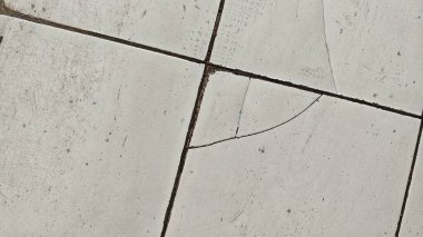 A close-up view of a cracked, dirty and broken white tile floor background. clipart