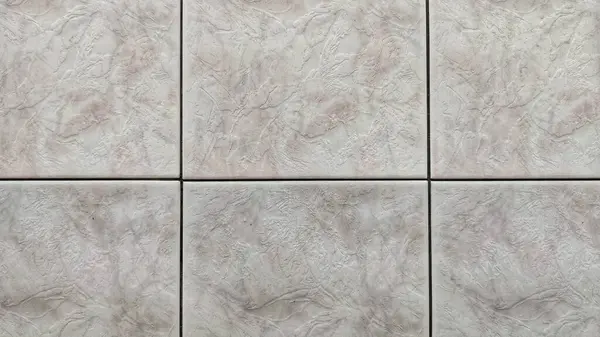 Seramik duvar fayanslarının yakın plan görüntüsü, ince girdaplar ve açık gri ve soluk pembemsi tonlarda doğal taş dokularını gösteren ızgara desenli düzende düzenlenmiş.