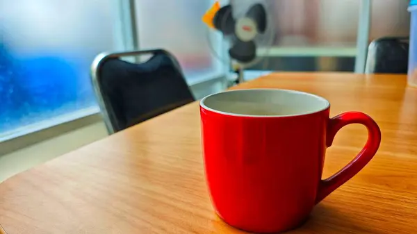 İçi beyaz, parlak kırmızı seramik bir kupa, ahşap bir masaya yerleştirilmiş.