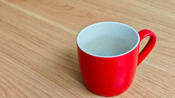 Parlak kırmızı bir seramik kupa. İçi beyaz, ahşap bir masaya yerleştirilmiş.