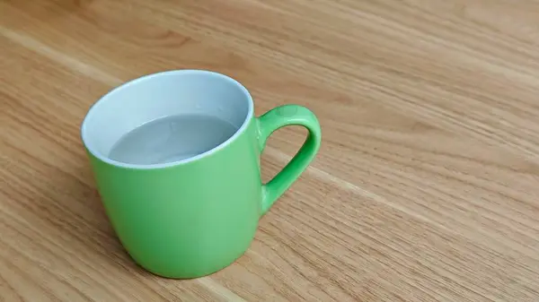 İçi su dolu, ahşap masaya yerleştirilmiş açık yeşil bir seramik bardak.