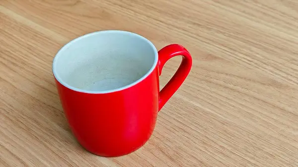 Parlak kırmızı bir seramik kupa. İçi beyaz, ahşap bir masaya yerleştirilmiş.