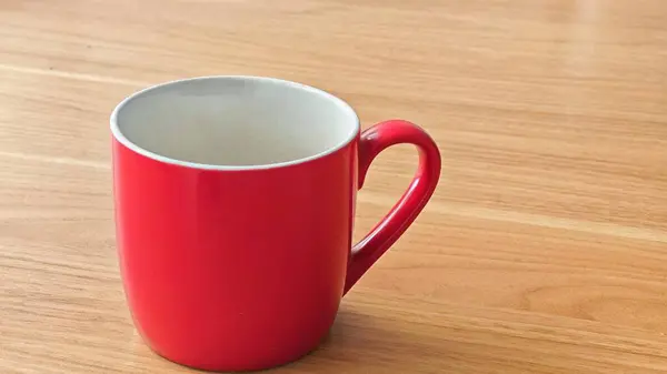 Parlak kırmızı bir seramik kupa. İçi beyaz, ahşap bir masaya yerleştirilmiş.