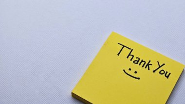 Gri arka planda izole edilmiş sarı yapışkan nottaki gülümseme ikonu ile teşekkür ederiz..