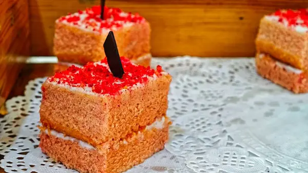 Üzerinde kırmızı kiraz olan bir dilim kahverengi sünger keki. Pasta üç parçaya bölünmüş ve beyaz bir kumaşın üzerinde duruyor.